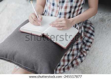 Beautiful young woman writing something in the note pad while lying on the floor at living room