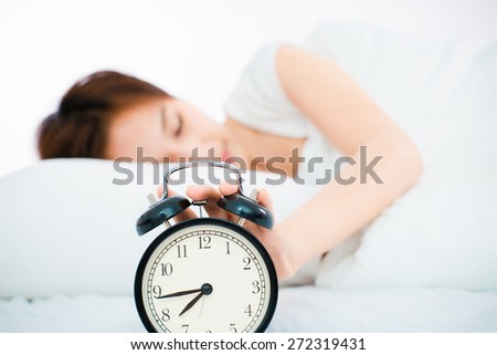 Woman in bed trying to wake up with alarm clock