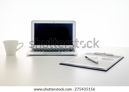 Still-life portrait of computer, pen, coffee mug on table, business report.