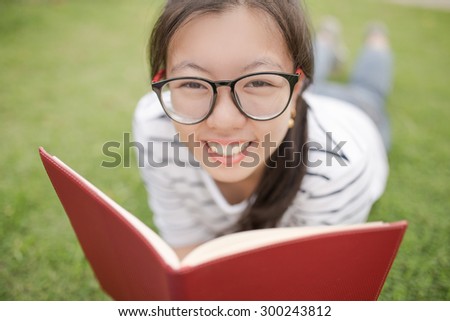 A female college student reading a book while lying on the park