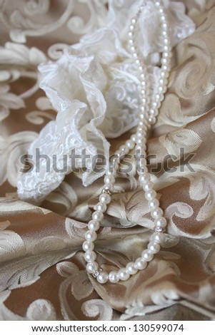 Pearl necklace and lace garter on gold silk patterned bedspread