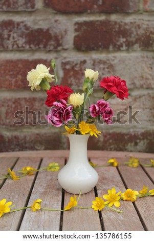 Carnations and celandines in white ceramic vase with celandine chain