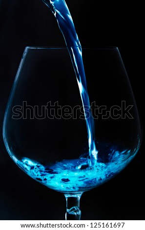 Blue liquid pouring to wine glass isolated on black