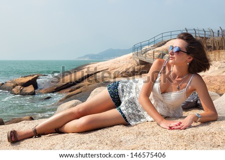 Young adult girl laying on the rock and look at the south china sea through sunglasses, Cheng Chau, Hong-Kong, China