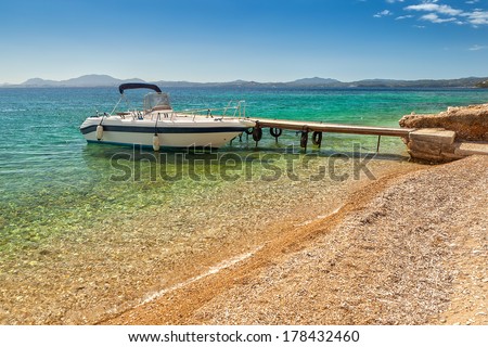 Empty boat standing at wooden pier under bright sunlight with shadow on pebbles at sea floor seen through transparent water of Ionian sea, Corfu, Greece