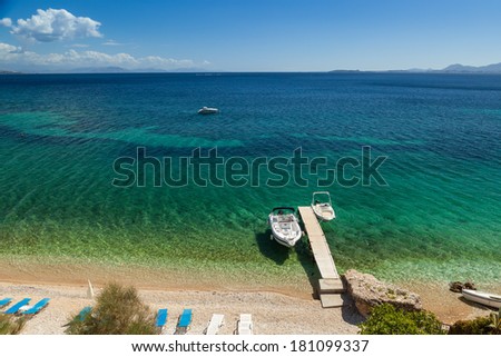 Empty boats standing at wooden pier under bright sunlight with shadow on pebbles at sea floor seen through transparent water of Ionian sea, Corfu, Greece
