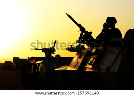 Silhouette Of Soldier With Machine Gun On A Car Against A Sunset