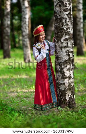 Funny girl in Russian dress in the Park is hiding behind a tree