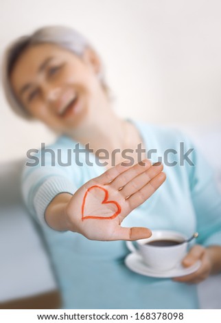 Happy blonde with a cup of coffee shows palm with a painted heart