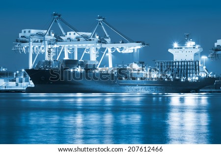 Cargo ship and crane at port reflect on river, twilight time (blue color tone).