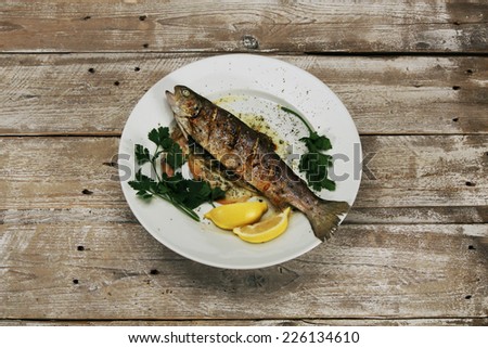 Baked fish (trout) on a white plate on vintage wooden desk - top view (also available as footage)