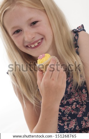 pretty blonde girl unwrapping and eating a fairy cake, isolated on white background