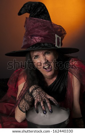Halloween witch with cauldron, casting spells on orange background