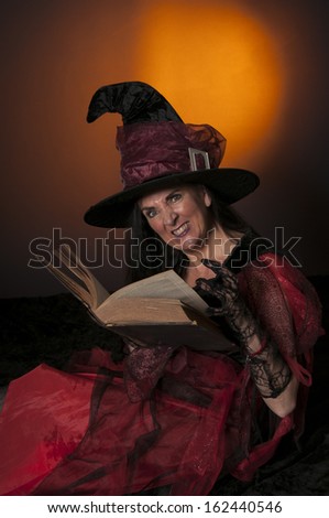 Halloween witch with book of spells on orange background