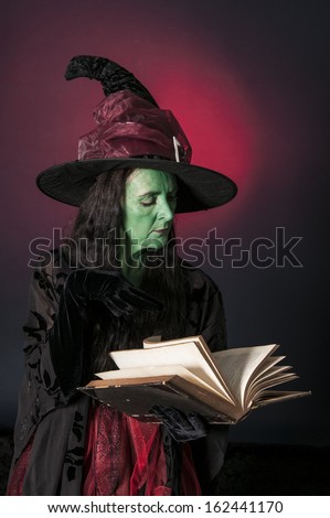 Halloween witch with book of spells on red background