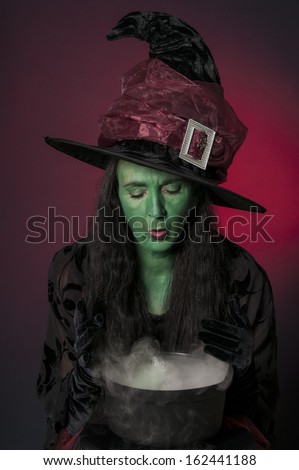 Halloween witch with green face and cauldron on red background