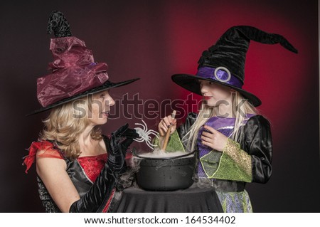 mother and daughter dressed as Halloween witches with cauldron isolated on dark red  background