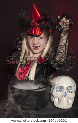 girl dressed as Halloween witch with skull and cauldron on dark red background