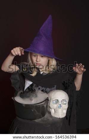 girl dressed as Halloween witch isolated with skull and cauldron on dark red background