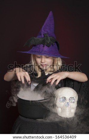 girl dressed as Halloween witch isolated with skull and cauldron on dark red background