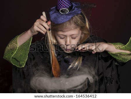 girl dressed as Halloween witch with cauldron isolated on dark red background