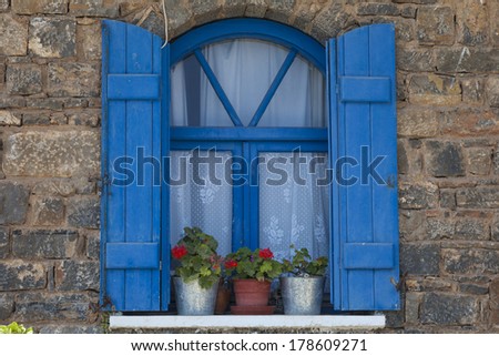 decorative window with blue painted shutters and red geraniums in pots  in Elounda, Crete