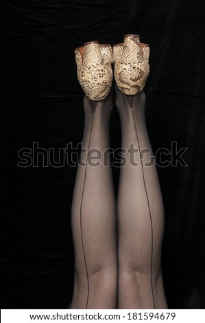 Vintage 1940 style woman in seamed stockings with her legs in the air, isolated on black background
