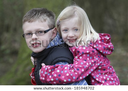 pretty girl having a piggy back on her brother\'s back  in woods