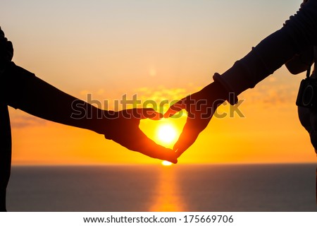 two hands of lovers on the background of sunset on the sea