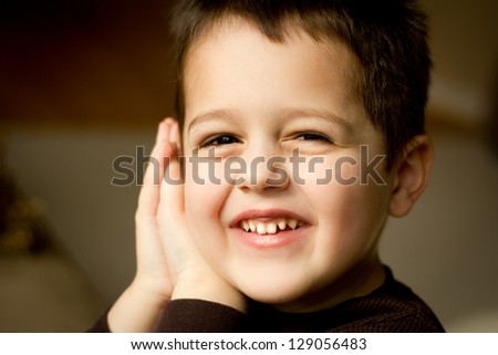 Close-up portrait of a cute little boy with brown hair and brown eyes smiling with his hands pressed to the side of his face.