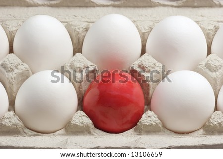Close up of white eggs and a red easter egg in a cardboard