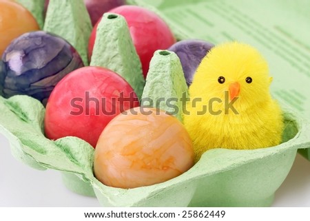 Colorful eggs in a carton with toy chicken