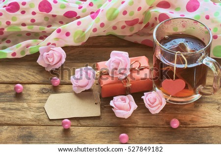 valentine\'s day composition cup with tea bag, paper tag, pink roses, beads on wooden table, retro toned image