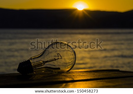 Bulb, lying on a wooden table, on background the bright sun, the mountains and the sea.