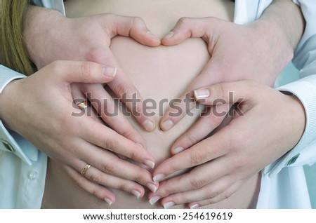 Four hands on a pregnant belly, close-up, Heart Shaped Pregnancy Portrait