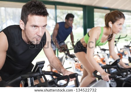 Two men and a woman are on fitness bicycles at a fitness center