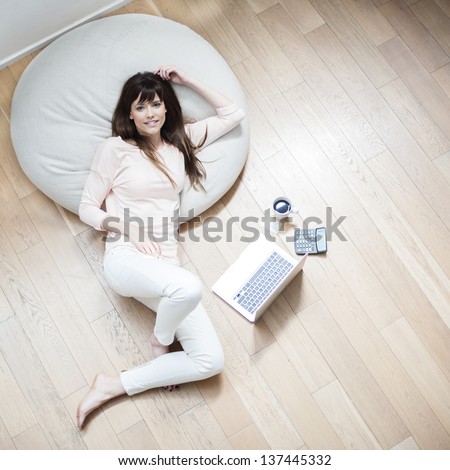 Portrait of a young woman lying on couch with laptop and cup of coffee