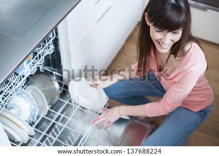 middle aged girl in the kitchen using dishwasher.  view of young woman in kitchen doing housework