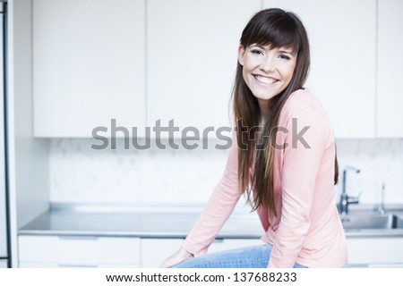 Relaxed young woman standing at the kitchen counter. Portrait of beautiful relaxed young woman standing at the kitchen counter - Indoor