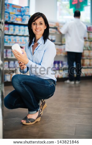 She is in the pharmacy. She is looking for some medicine. We can see the pharmacist in the background