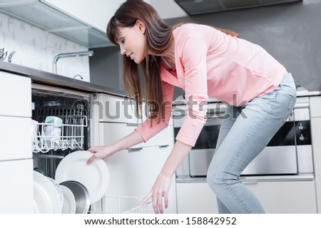 A beautiful woman using a dishwasher in a modern kitchen. domestic appliance