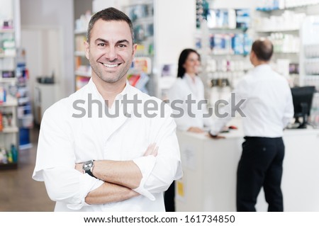 Portrait Of A Pharmacist. In The Background We Can See To A Customer Served By Another Pharmacist