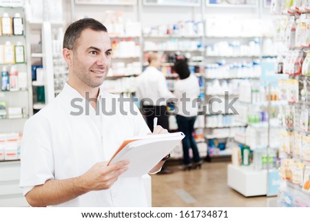 Pharmacist taking notes in a notebook. In the background we can see two customers at the pharmacy