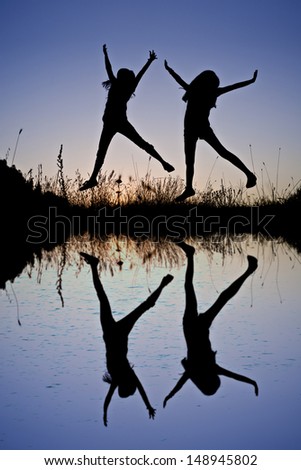 Reflection in lake  and silhouette of friends jumping in sunset