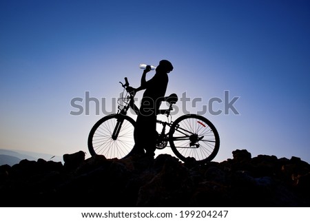 Cyclist drinking water. Silhouette of a man on mountain bike at sunset