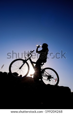 Cyclist drinking water. Silhouette of a man on mountain bike at sunset