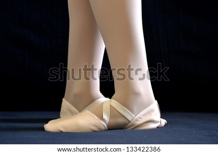 Ballet feet in pink leather slippers standing in fifth position from calf down on black background