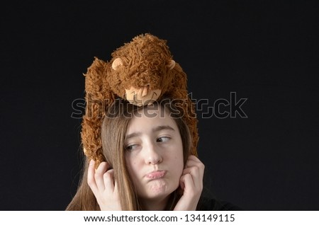 Teen with sad expression holding stuffed monkey peeking over her head