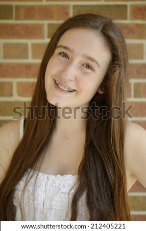 Pretty teen girl with long brown hair and braces smiling with brick background