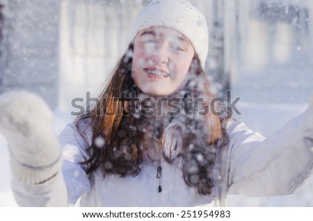 Pretty brunette girl outside in the winter  wearing white knit hat and mittens behind falling snow